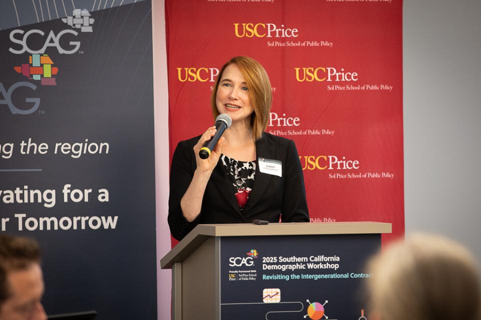 Woman speaking at a podium, red and blue banners in background.