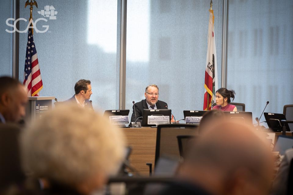 Business meeting with three people at a conference table, flags in background.