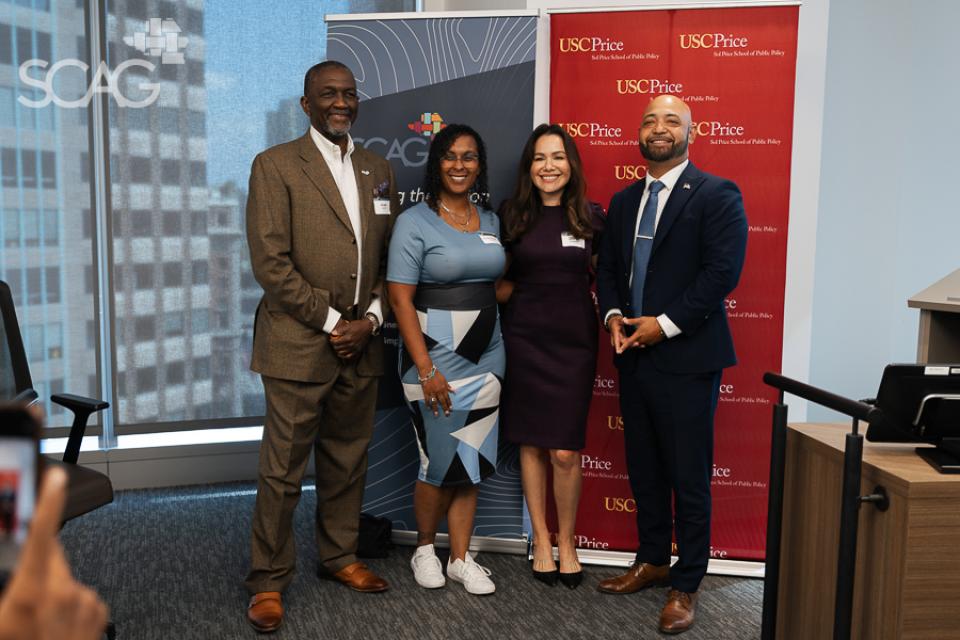 Four people standing together, smiling in a conference room.
