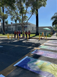 Colorful crosswalk and people in orange vests on a sunny street.
