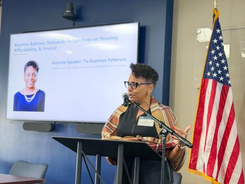 Speaker at podium with U.S. flag, presenting on housing affordability.