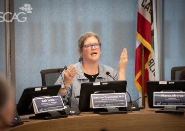 Woman speaking at a conference table with multiple microphones.