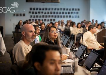 People seated in a conference room, focused on a presentation.
