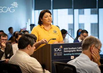 Speaker at a podium in a meeting room, wearing a yellow shirt.