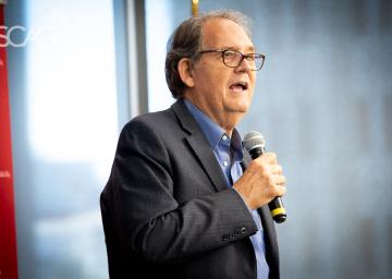 Man speaking into a microphone in a bright room.