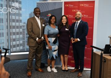 Four people standing together, smiling in a conference room.