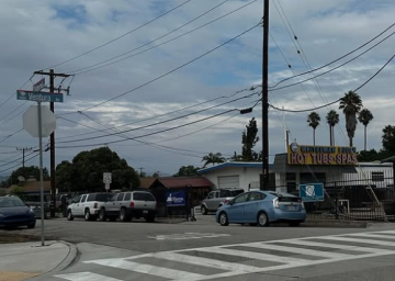 Street corner with parked cars, power lines, and cloudy sky.