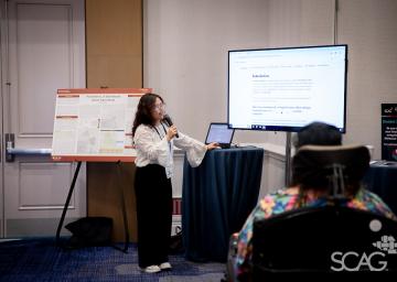 Presenter with microphone near a screen in a conference room.