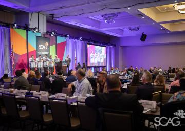 Conference event with seated attendees, colorful stage, and presentation screen.