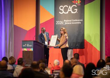 Award presentation at SCAG conference with a colorful geometric backdrop.