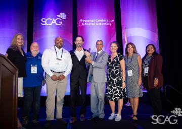 Eight people on stage smiling against a purple backdrop with "SCAG" logos.