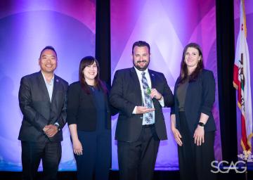 Four people in suits smiling on stage with a purple background.