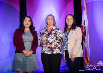 Three women standing together, smiling, with a purple backdrop.