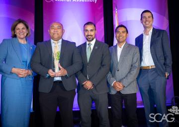 Five people in formal attire smiling on a stage with a purple backdrop.
