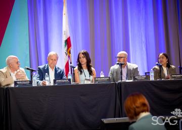 Panel of five people speaking at a conference, seated behind a table.