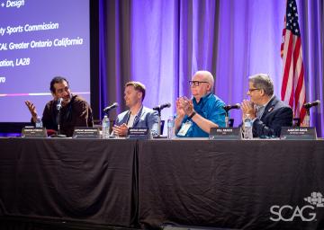 Panelists sit at a table with microphones and water bottles, engaged in discussion.