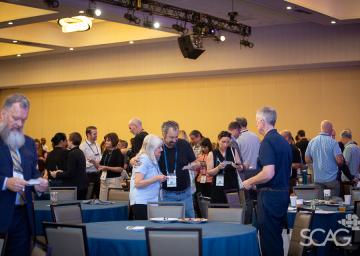 Conference attendees networking in a large room with round tables.