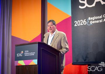 Man in a suit speaking at a podium with colorful backdrop.