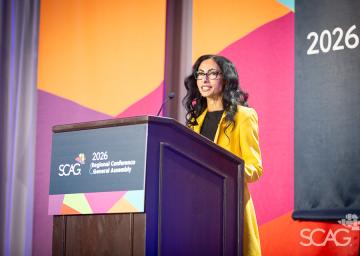 Woman speaking at a podium in a conference setting with colorful backdrop.