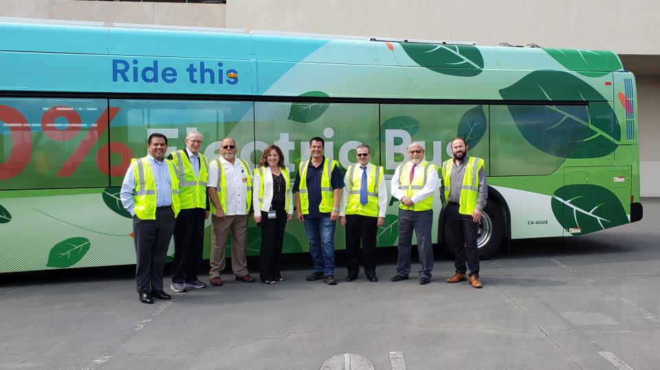 A group of people in yellow safety vests stand in front of an electric city bus.